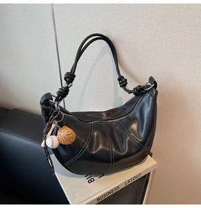Detailed close-up of a black leather crescent bag featuring white contrast stitching