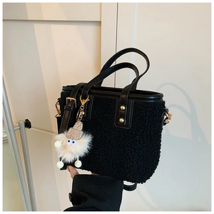 Detail of plush black bucket bag with leather handles and cute white mascot charm