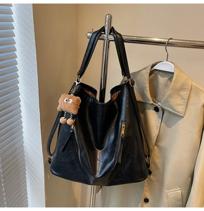 Detail of black PU leather tote bag with gold zippers and brown plush charm accessory