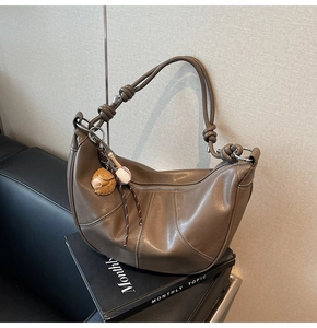 Detail view of brown dumpling bag with curved stitching and baseball charm