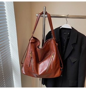 Detail of vintage brown leather tote bag with dual front zippers on metal hanger