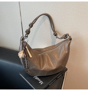 Detail of a brown leather crescent bag featuring knot strap and baseball charm
