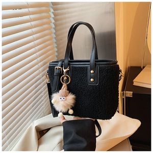 Close-up of black plush bucket bag with leather handles and a cute pom-pom doll charm