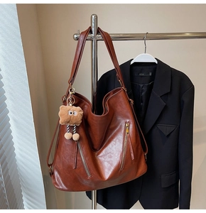 Macro detail of retro brown leather tote with metal zippers and cute plush charm pendant