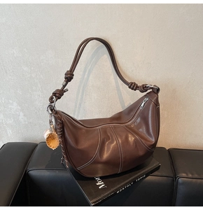 Detail view of brown leather crescent bag showing white contrast stitching and knots