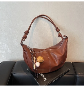 Detail of dark brown lychee leather hobo bag with baseball charm and knot handle