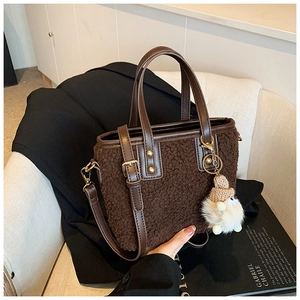Detail of dark brown plush bucket bag with leather strap and a cute doll pendant