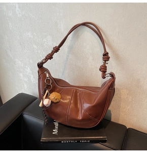 Detailed close-up of brown leather crescent bag with unique knotted strap and baseball charm