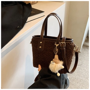 Detail of faux shearling bucket bag with brown leather handles and plush monster charm