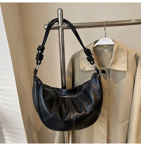 Detail of black crescent shoulder bag with white contrast stitching and knotted strap