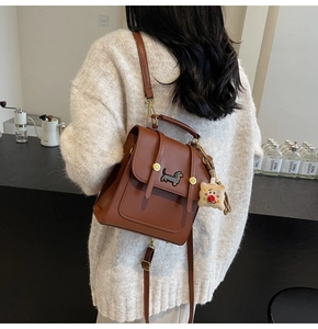Brown leather backpack featuring dachshund embroidery and plush toast charm in cafe setting