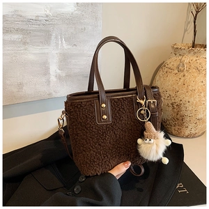 Detail of dark brown plush bucket bag with leather handles and a cute fuzzy charm