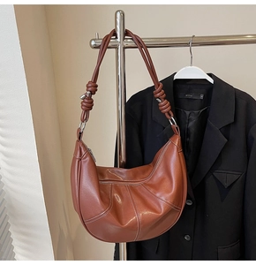 Detail showing brown half-moon shoulder bag with white contrast stitching and knotted strap