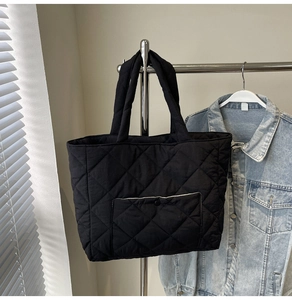 Detail of black quilted tote bag showing diamond stitch patterns and front snap pocket