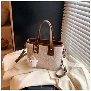 Detail of cream sherpa bucket bag with brown leather handles and a plush eye charm