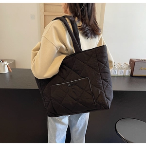 Close-up of black quilted tote bag with front pocket and shoulder strap on model