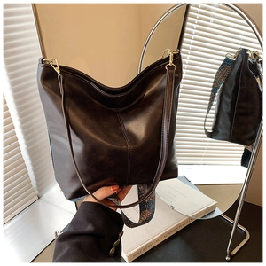 Detail of dark brown leather bucket bag with vintage pattern wide strap and gold hardware