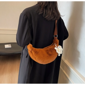 Detail view of brown plush crescent bag with fuzzy doll pendant on a black coat