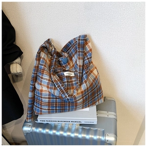 Détail du sac cabas à carreaux avec écusson cœur bleu sur une surface métallique