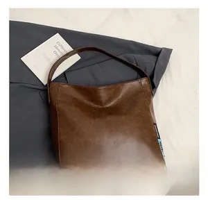 Detail of a large dark brown PU leather tote bag styled over a grey blazer and props