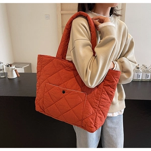 Close-up of quilted brick red tote bag with large outer pocket and button detail