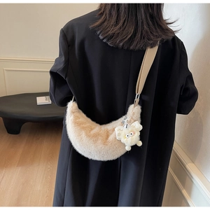 Detail of plush beige crescent shoulder bag with fuzzy cartoon charm and wide strap