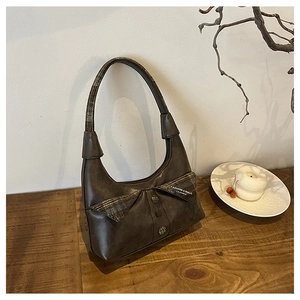 Detailed view of brown vintage leather shoulder bag with bow knot on wooden desk