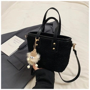 Detail of black plush bucket bag with leather handles, gold rivets and a cute doll charm