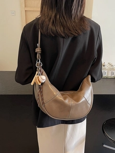 Brown leather hobo bag with contrast stitching and baseball charm shown on model
