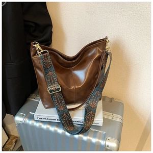 Detail of a brown leather tote bag with a vintage patterned strap and gold hardware