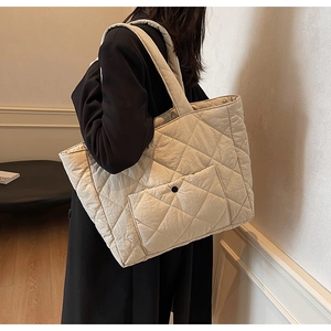 Detailed macro view of large quilted puffer tote bag with front pocket and snap button