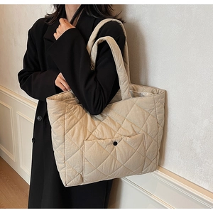 Detail of beige quilted tote bag with diamond pattern and decorative snap pocket