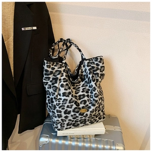 Detailed close-up of leopard print tote bag with gold metal plate on a silver suitcase