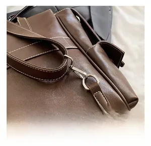 Detailed close-up of premium silver metal hooks and white stitching on brown leather bag