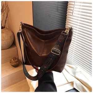 Detail of vintage brown leather tote bag featuring a bohemian style woven shoulder strap