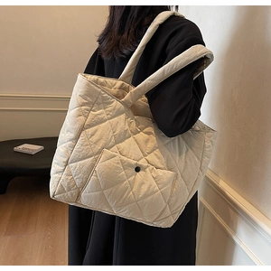 Detail of quilted diamond pattern and front flap pocket on a beige puffer tote bag