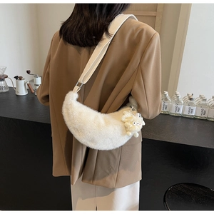 Detail of plush off-white crescent crossbody bag with monster charm and wide strap