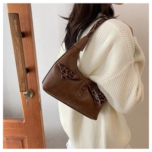 Detail of dark brown leather underarm bag with leopard print strap and retro buttons
