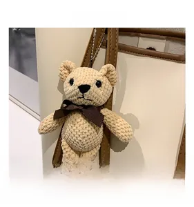 Detail of a beige knitted bear charm with a brown bow attached to a tote bag