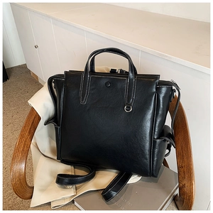 Detail of black faux leather tote bag with white contrast stitching on a wooden chair