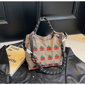 Nahaufnahme der braunen Canvas-Tasche mit Kirschstickerei und geflochtenen Griffen