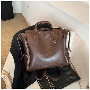 Detailed view of dark brown leather backpack featuring contrast stitching on a beige chair