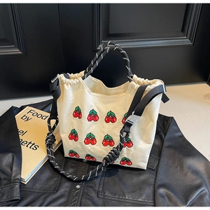 Detail der cremefarbenen Canvas-Tasche mit roten Kirschstickereien und Webgriffen