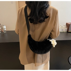 Detail of a soft black faux fur crescent bag with a white plush charm worn on shoulder