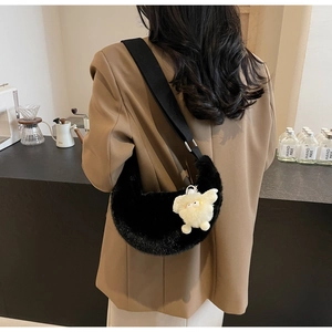 Black plush crescent shoulder bag with white lamb pendant shown in a city cafe setting