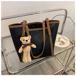 Close-up of black tote bag with brown leather straps and cute beige bear charm pendant