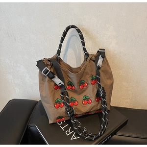 Detailaufnahme der braunen Canvas-Tasche mit Kirschstickerei und gewebten Riemen