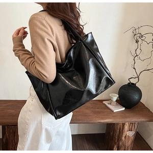 Grand sac cabas en cuir verni noir brillant porté à l'épaule dans un décor épuré