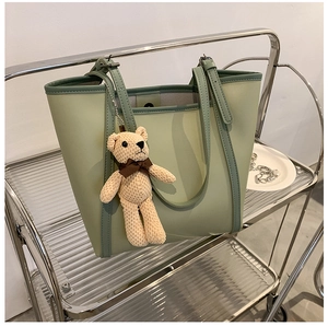 Detail of light green contrast tote bag with a cute bear pendant on a metal shelf
