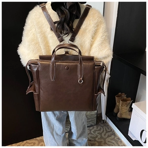 Detailed view of deep brown vintage backpack featuring contrast white stitching and metal ring